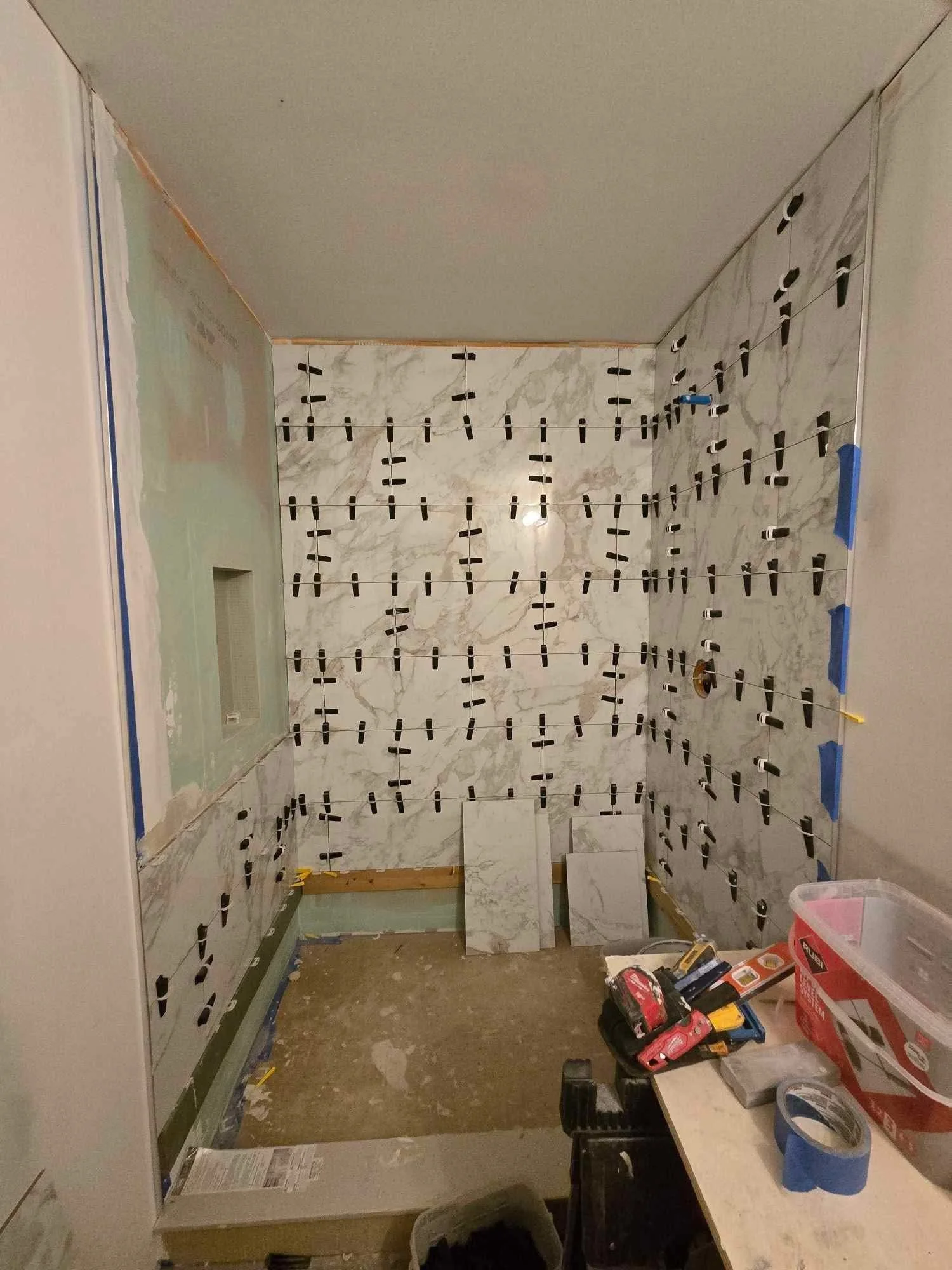 A room under renovation with marble wall tiles being installed using spacers, construction tools on a table, and partially finished walls.