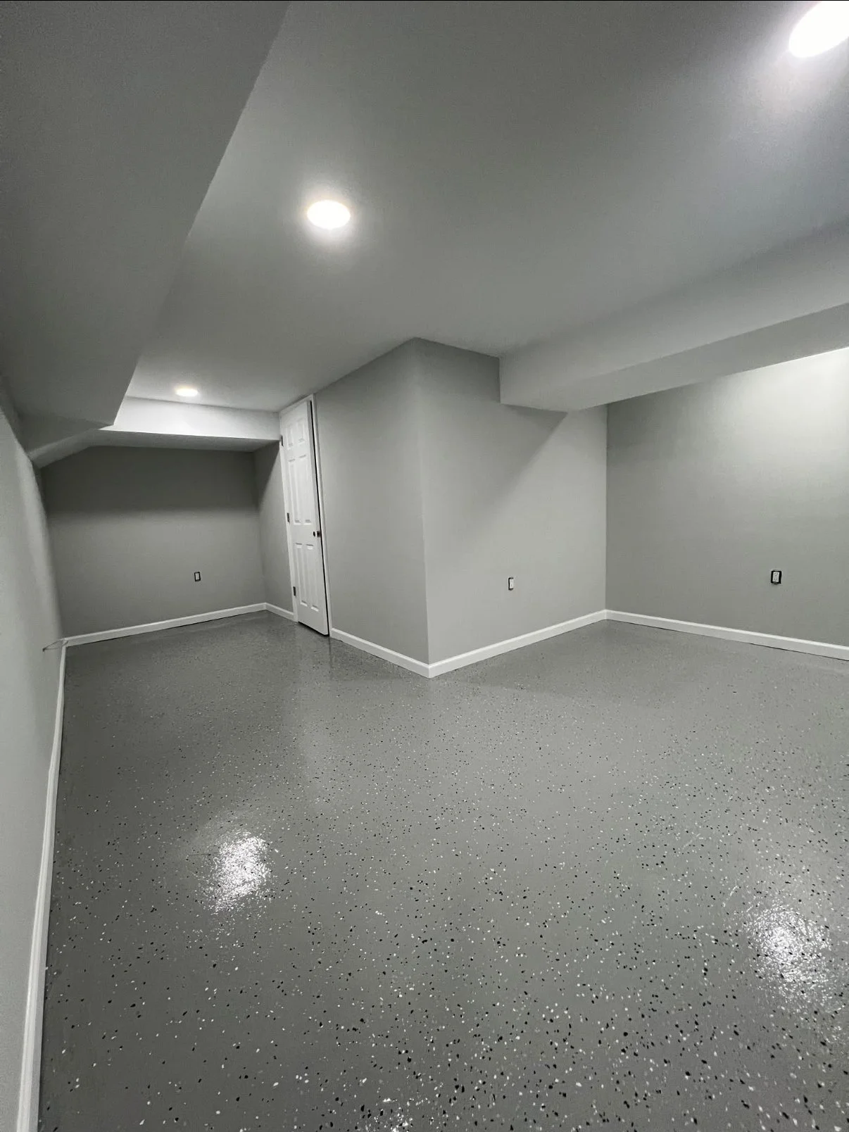 Empty basement room with gray speckled epoxy floor, white walls, and ceiling with recessed lighting.