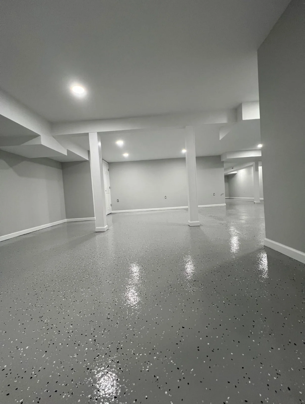 Empty, clean basement with gray speckled epoxy flooring, white walls, and recessed ceiling lights.
