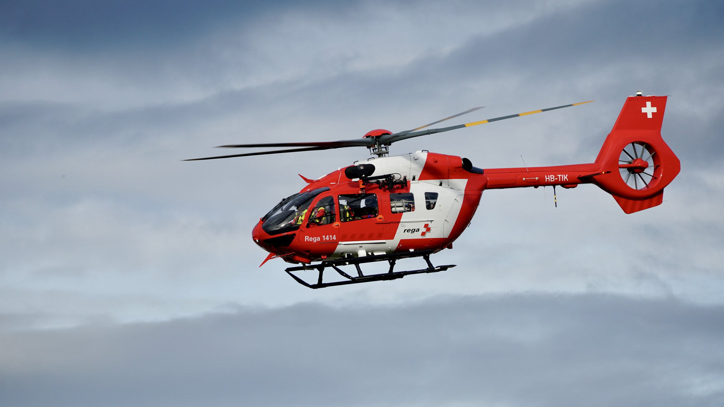 Rot-weisser Rettungshelikopter fliegt in den Himmel unter bewölktem Himmel.