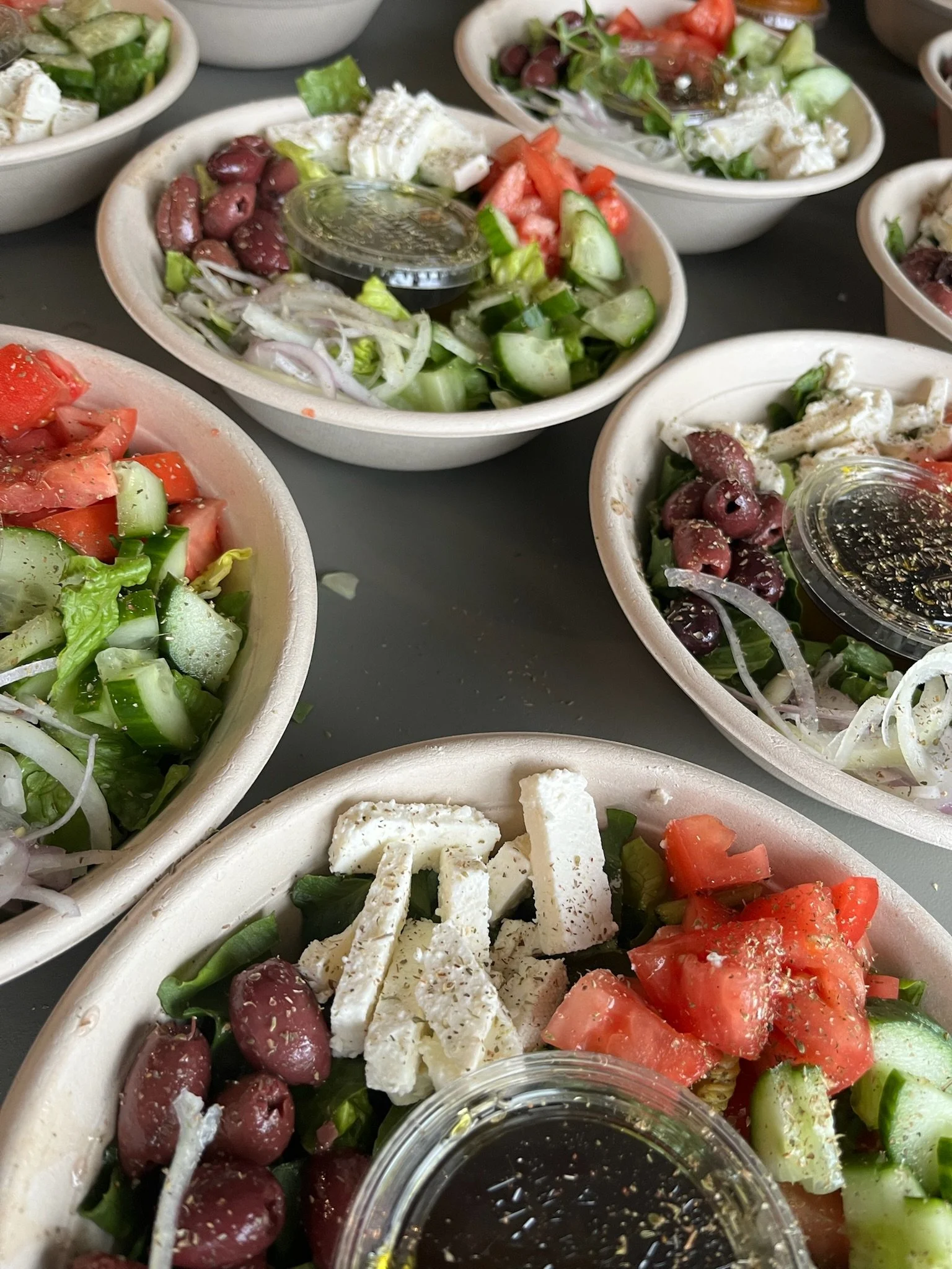 Several bowls of Greek salads with tomatoes, cucumbers, onions, olives, feta cheese, and dressing.