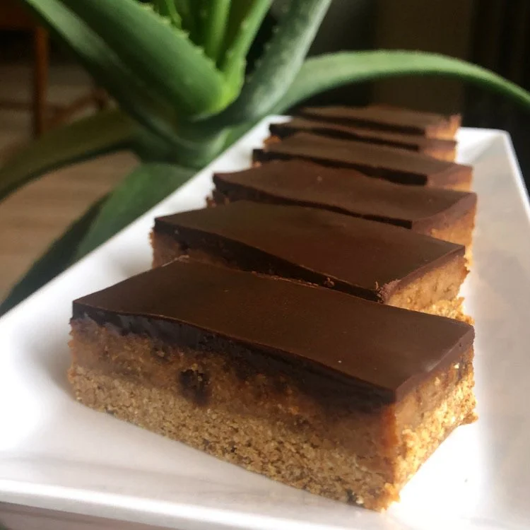 Several slices of chocolate-topped dessert with a crumbly base on a white plate, with a pineapple plant in the background.
