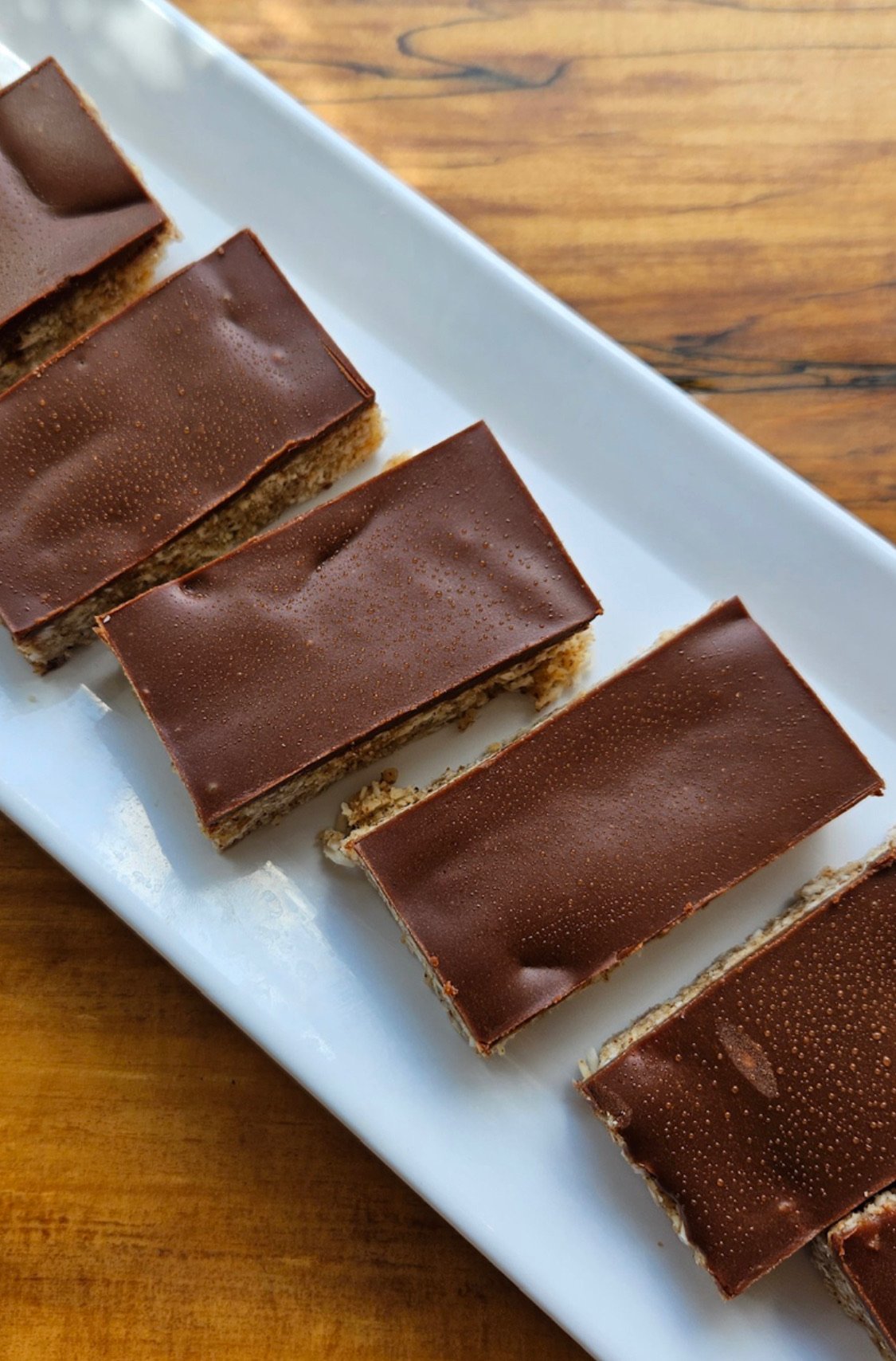 Chocolate-covered bars on a white platter, placed on a wooden surface.