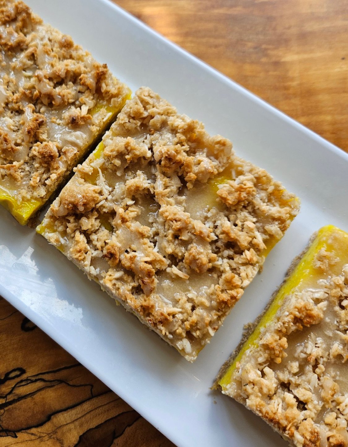 Close-up of lemon bars with a crumbly topping on a white rectangular plate.