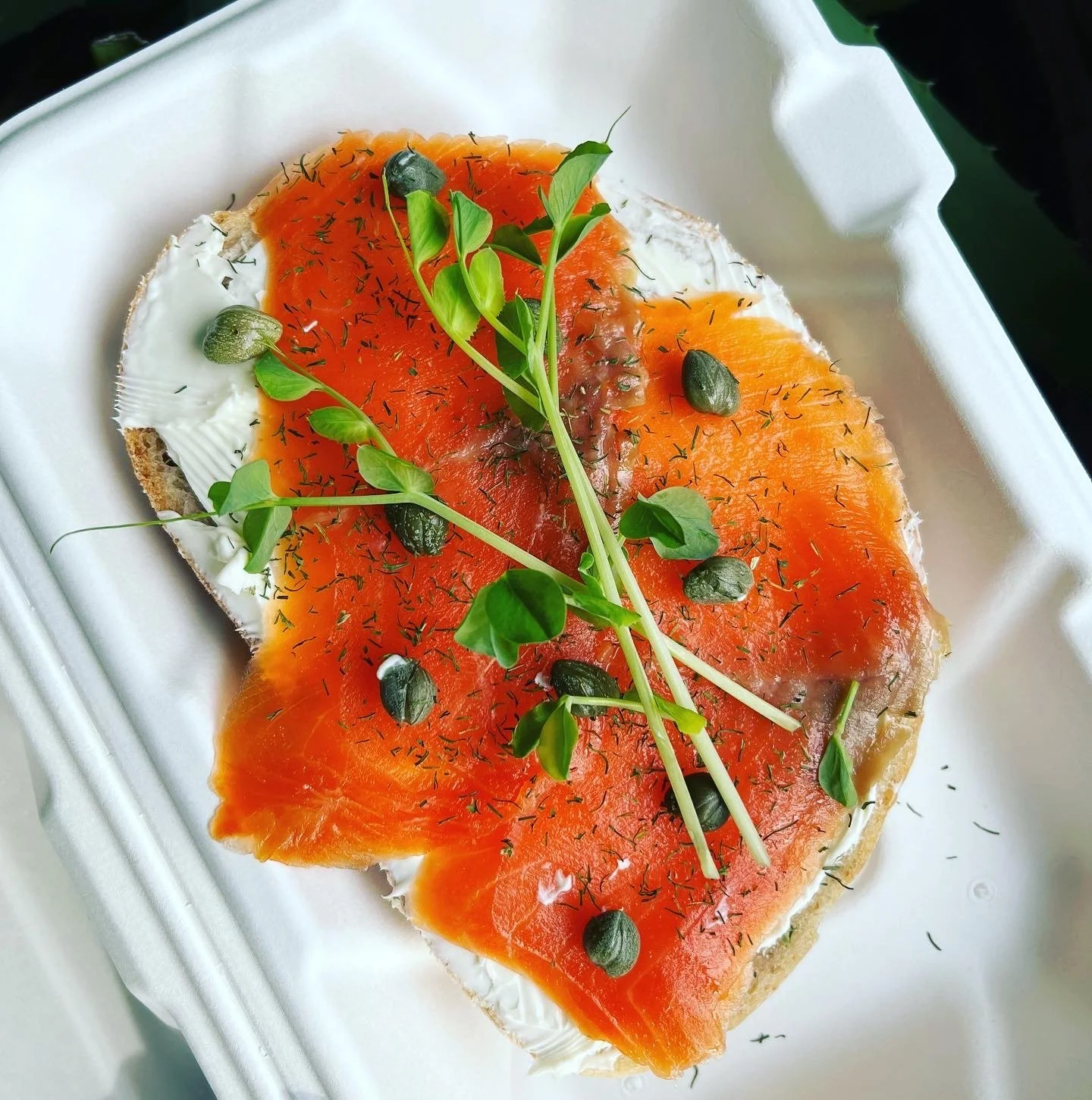 Open-faced sandwich with smoked salmon, cream cheese, fresh greens, capers, and dill on a slice of bread.