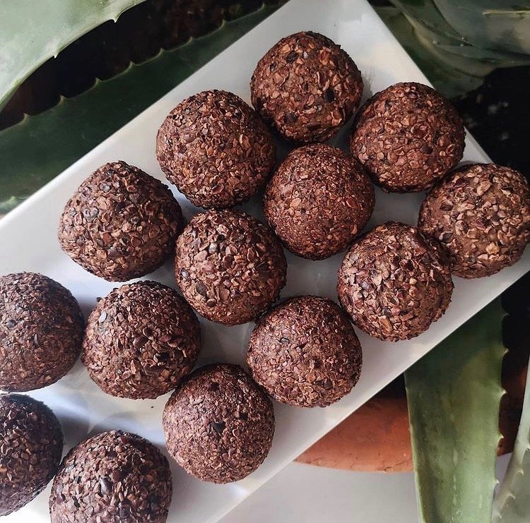 A white rectangular plate with chocolate energy balls coated with crushed nuts or grains, arranged in two rows.