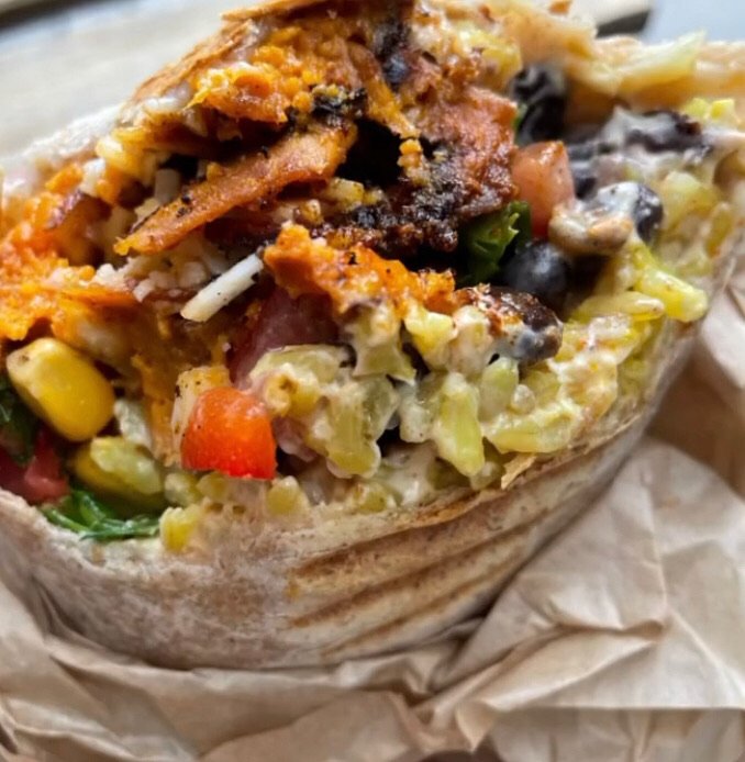 Close-up of a burrito filled with rice, black beans, corn, lettuce, shredded cheese, and seasoned meat, wrapped in a soft flour tortilla.