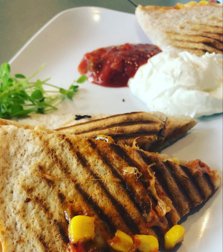 Grilled quesadilla with corn and cheese, served with salsa, sour cream, and garnish on a white plate.