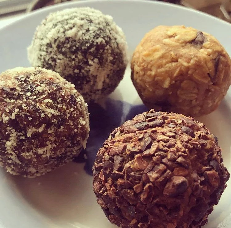 Four assorted chocolate truffles on a white plate.