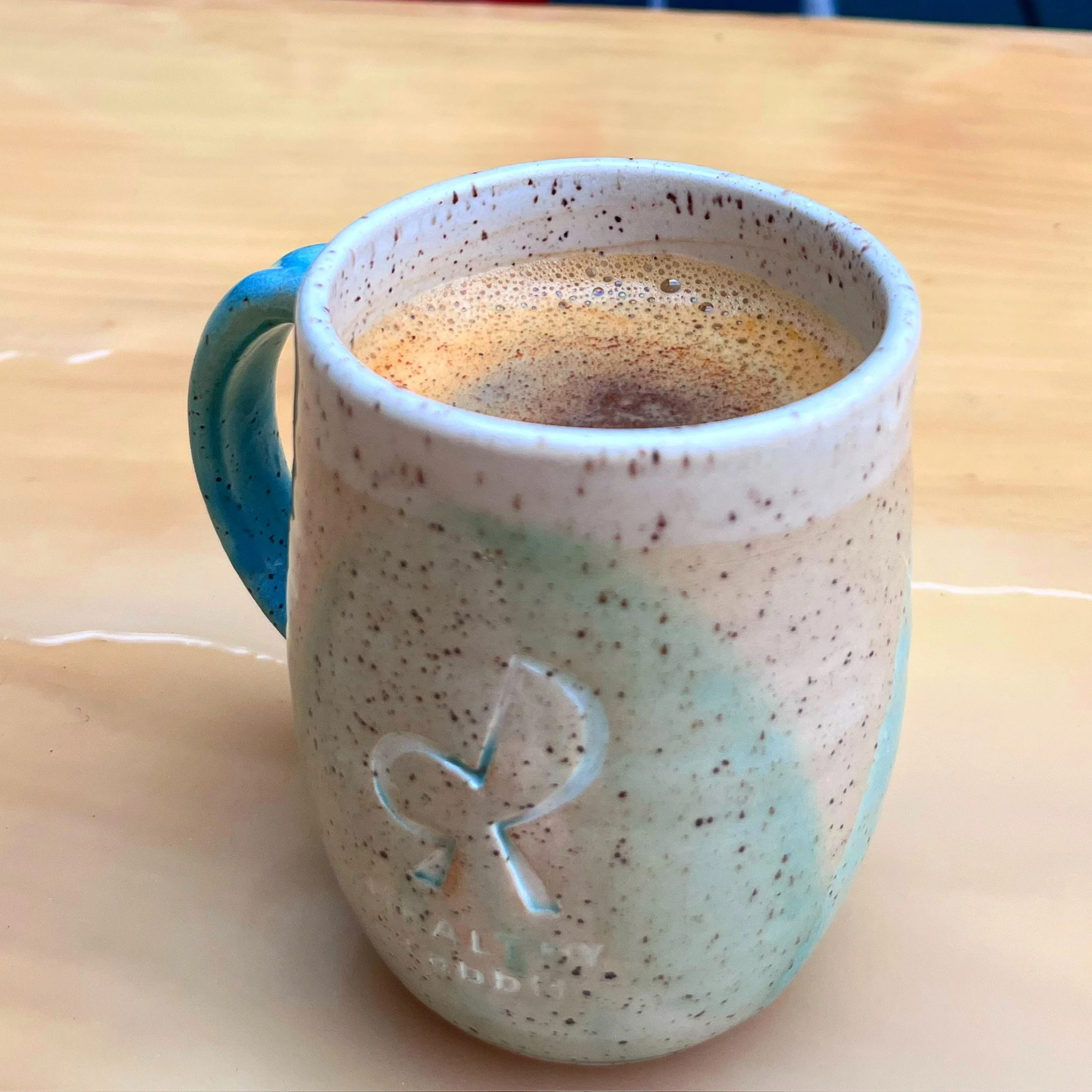 A ceramic mug filled with a frothy coffee drink, sitting on a wooden surface.