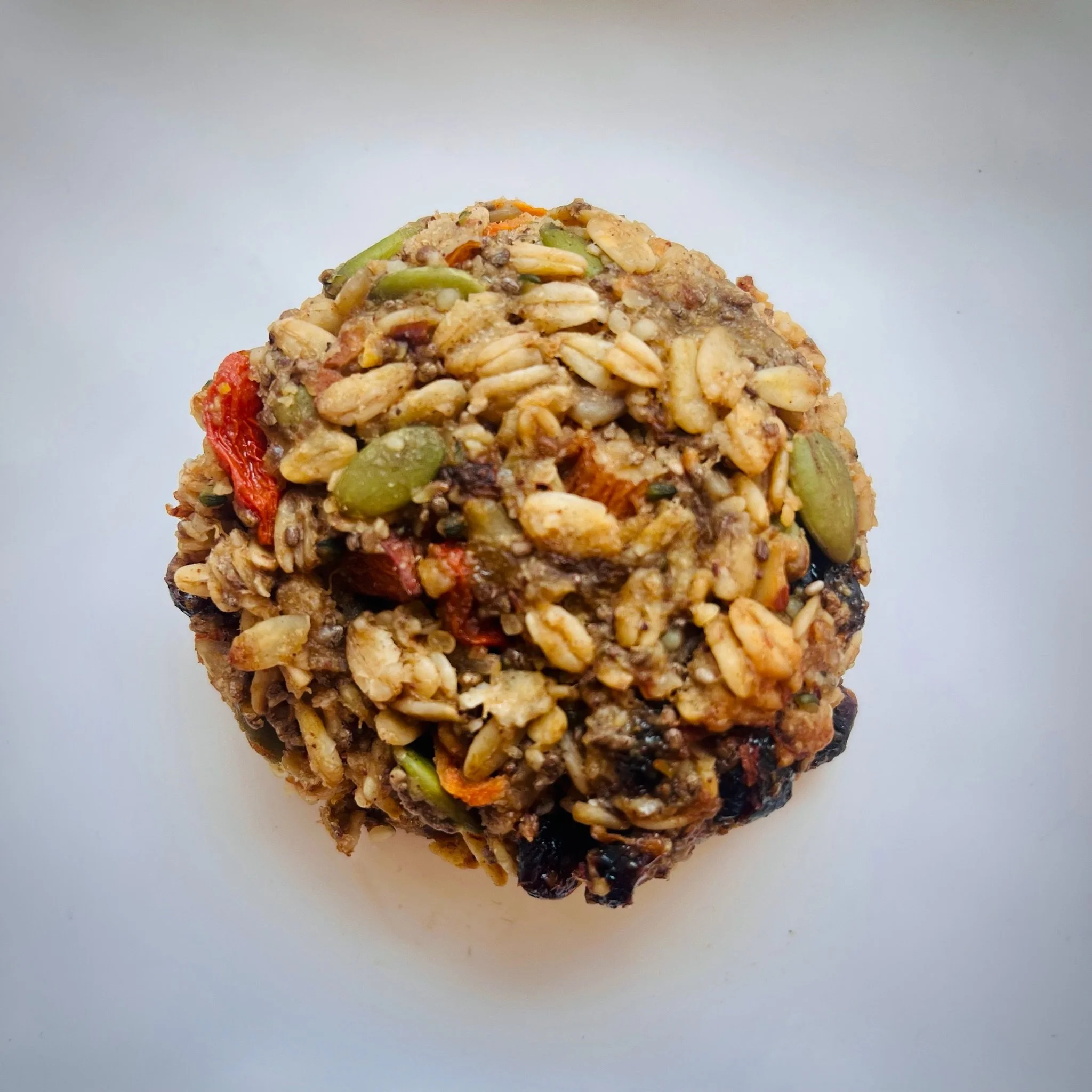 Close-up of a homemade granola ball containing oats, seeds, dried fruit, and nuts on a white background.