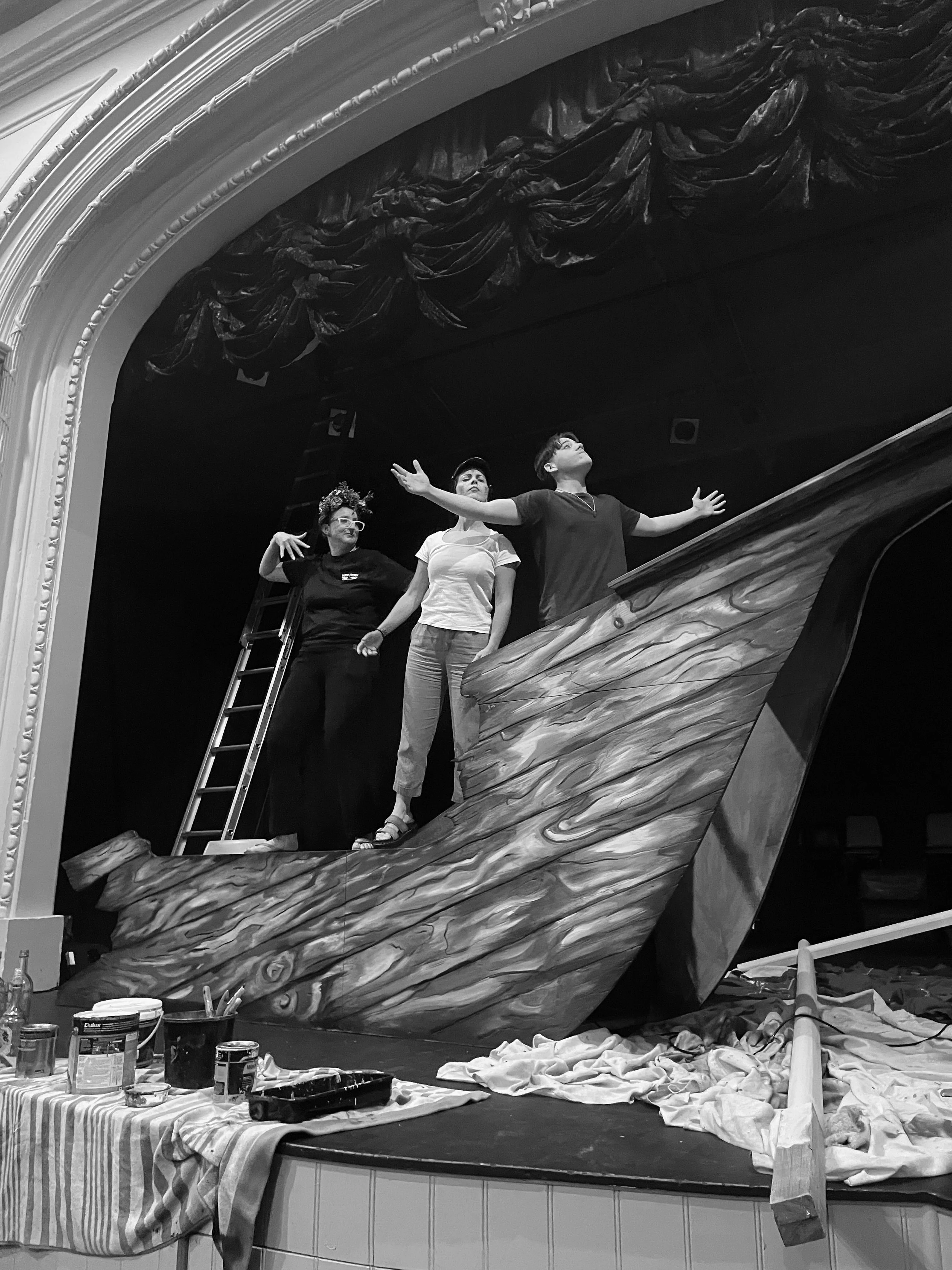 Three performers on stage around a large wooden boat set piece during a Perth French Theatre production.