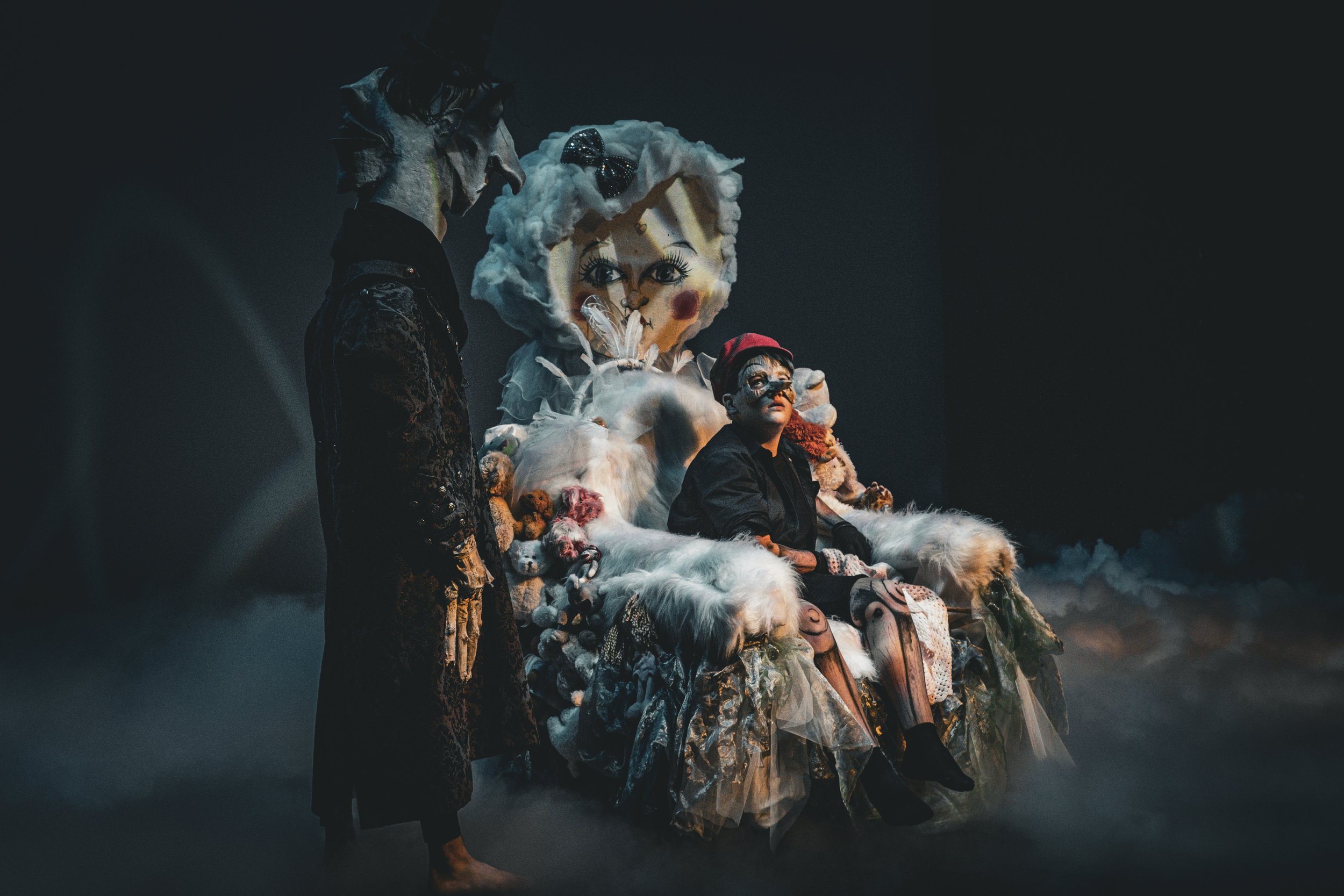 Two Perth French Theatre performers beside an elaborately costumed seated character on stage.