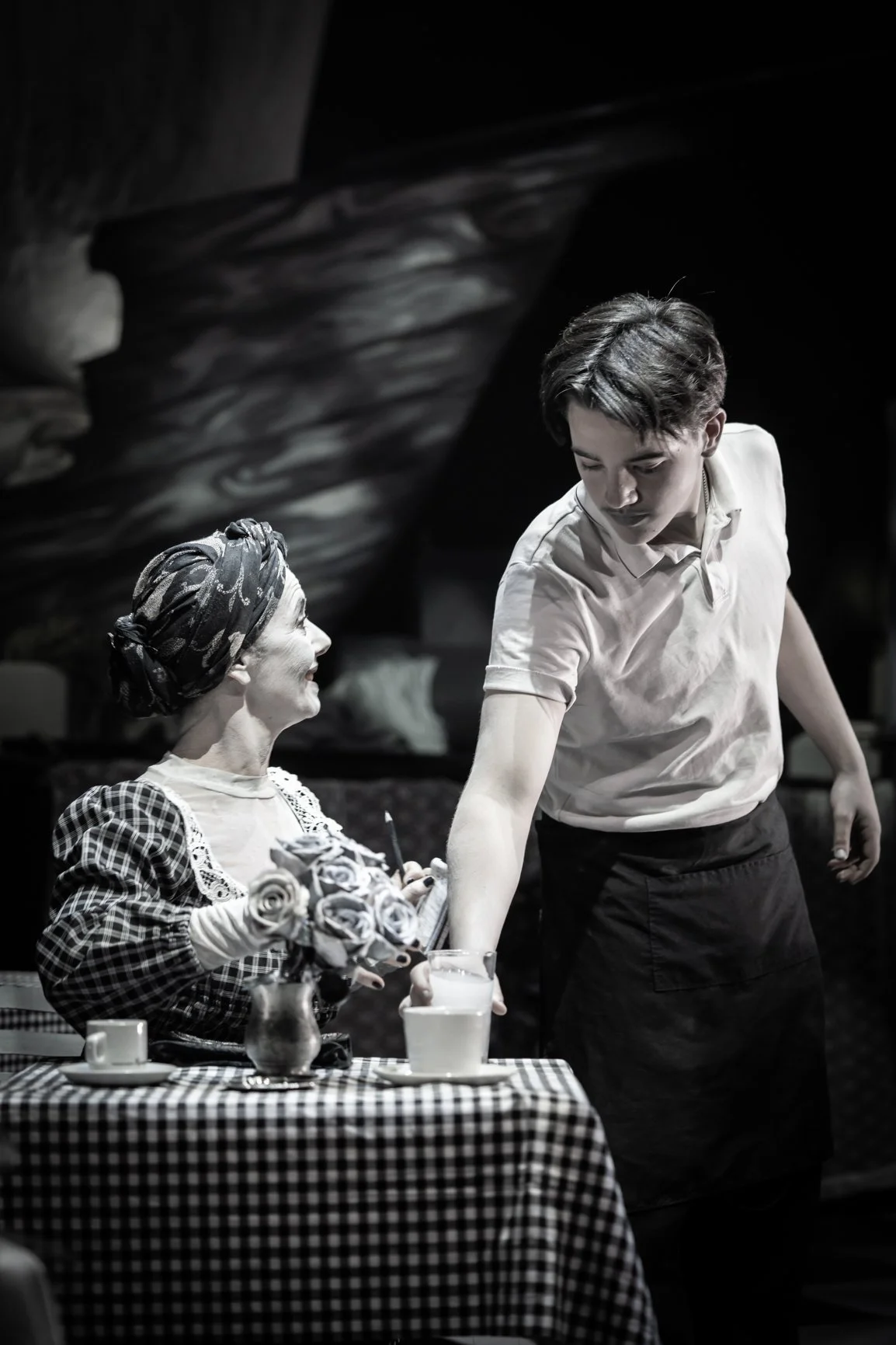 Two performers facing each other across a table during a Perth French Theatre production.