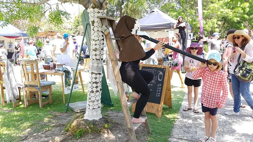Performer dressed as a whispering bird sharing poetry with a child through a long tube at Bonjour Perth Festival.