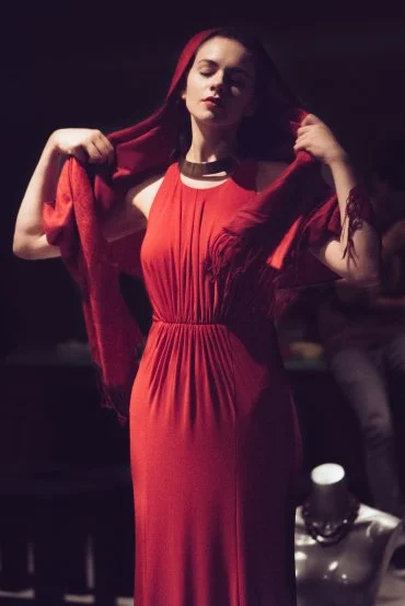 Performer in a red dress standing on stage with her eyes closed during a Perth French Theatre production.
