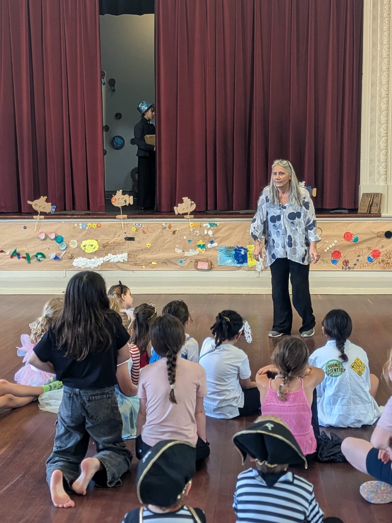 Children sitting on the floor watching the facilitator during a French Holiday Program activity in Perth.