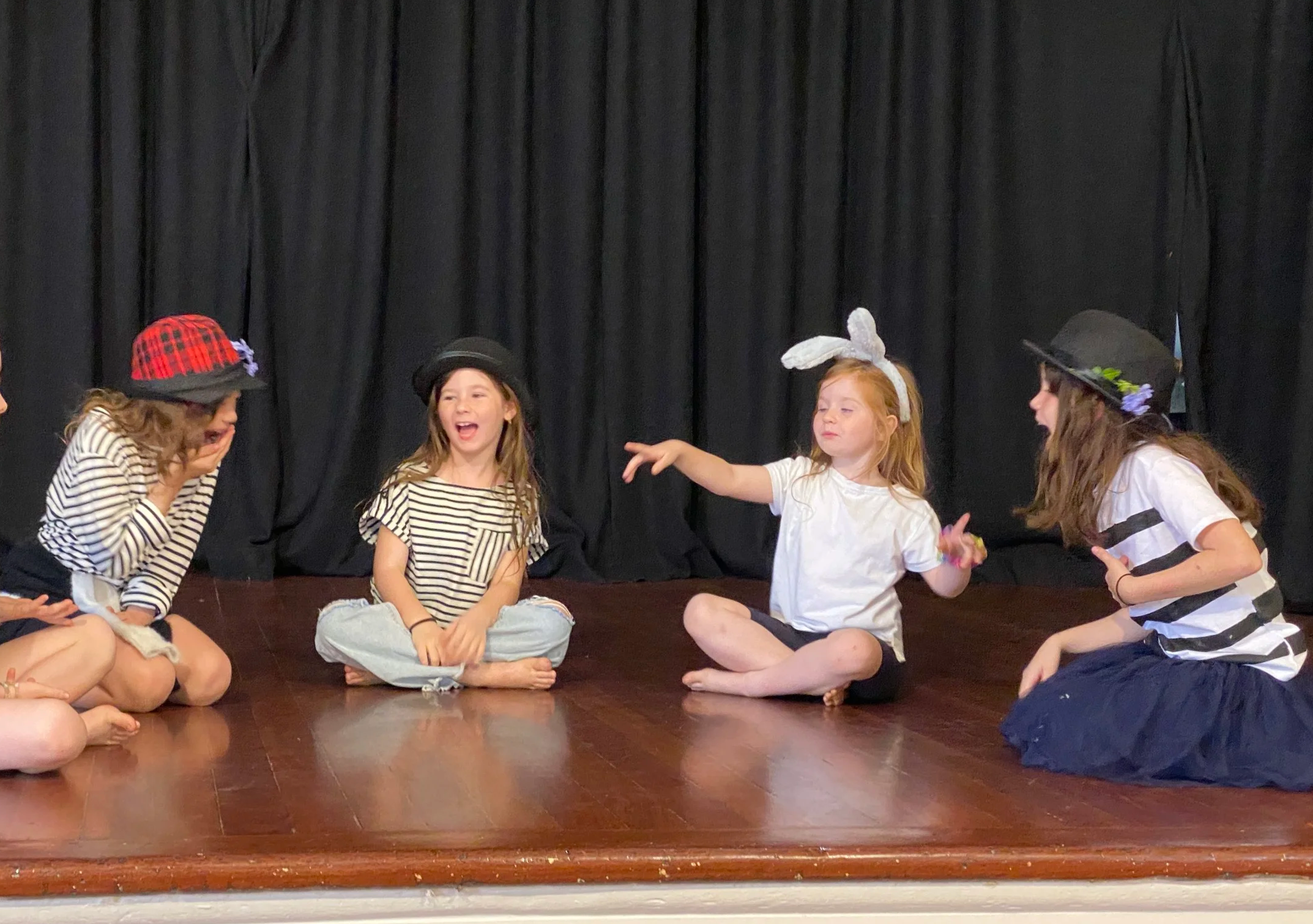 French Holiday Program children sitting together on stage during a theatre activity.