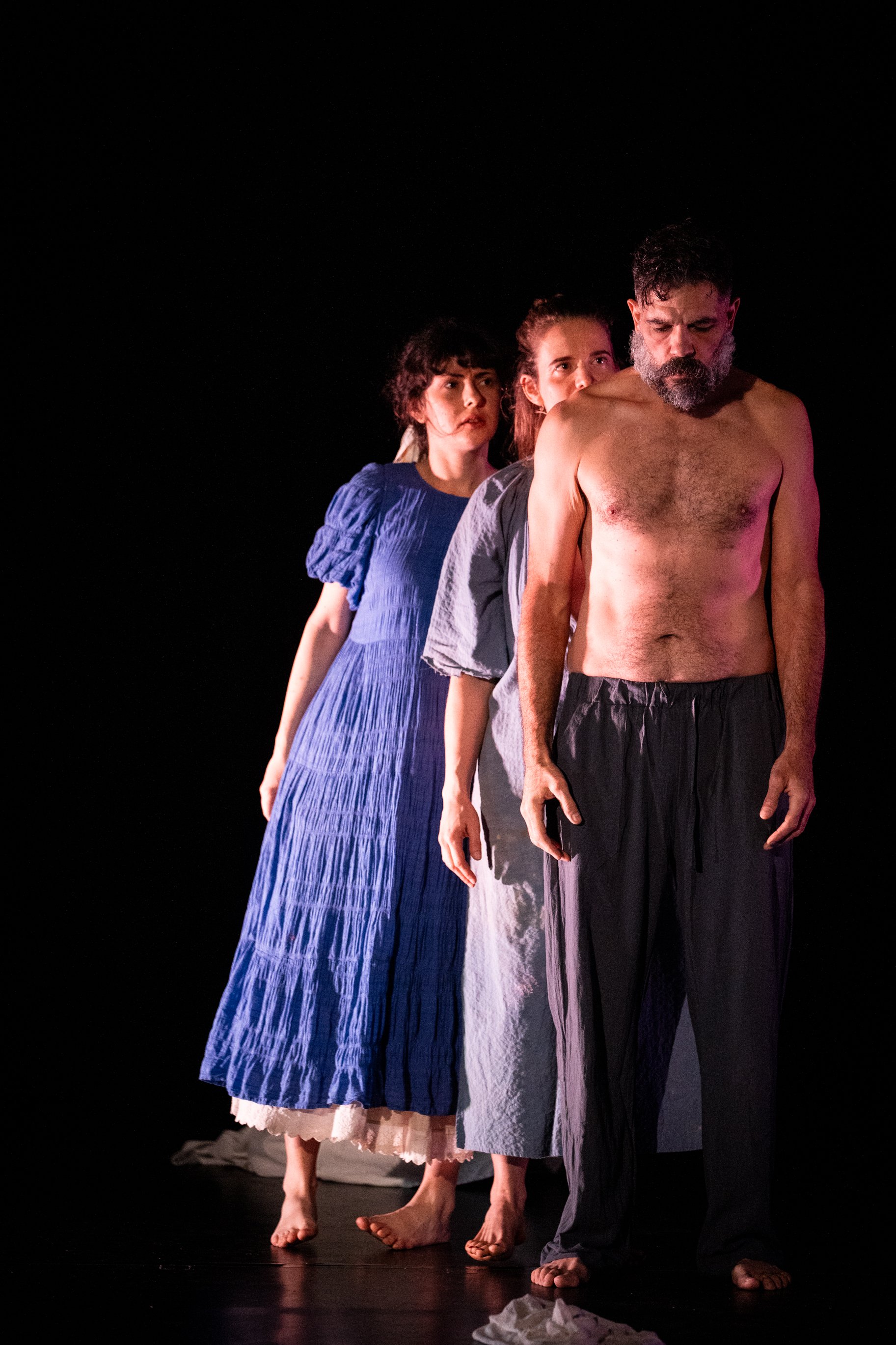 Three Perth French Theatre performers standing barefoot on stage against a dark background.
