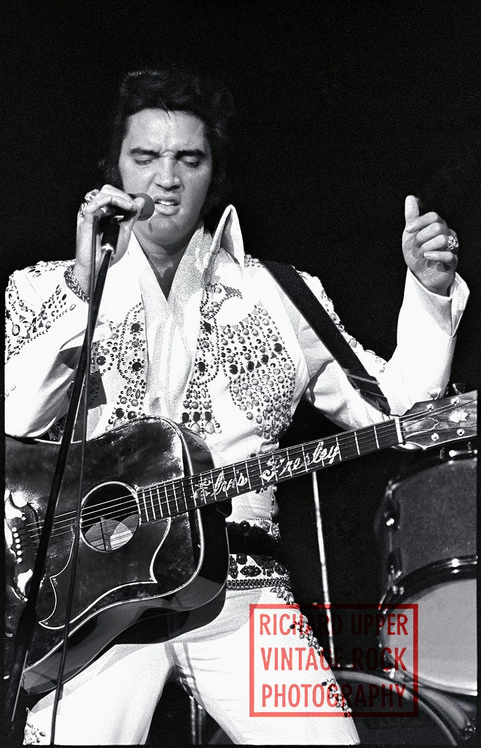 Black and white photo of Elvis Presley performing with a microphone and guitar.