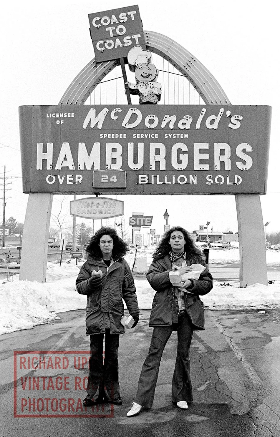 Two women standing in front of a vintage McDonald's sign advertising millions of hamburgers sold, with snow on the ground and a few buildings and signs in the background.