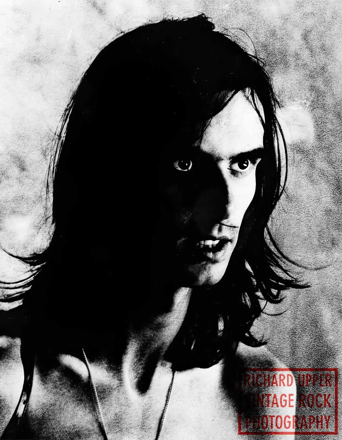 Black and white portrait of a woman with shoulder-length hair, intense expression, and minimal clothing, with a textured background and a red stamp-like logo reading "Richard Upper Vintage Rock Photography" in the bottom right corner.