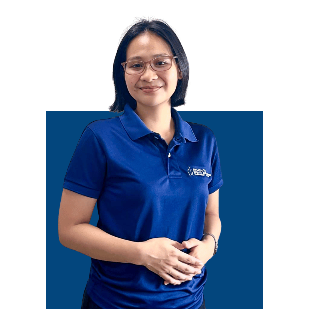 A woman with glasses and shoulder-length black hair, wearing a blue polo shirt with a logo, standing against a background with a white upper section and a dark blue lower section, smiling and holding her hands together in front of her.