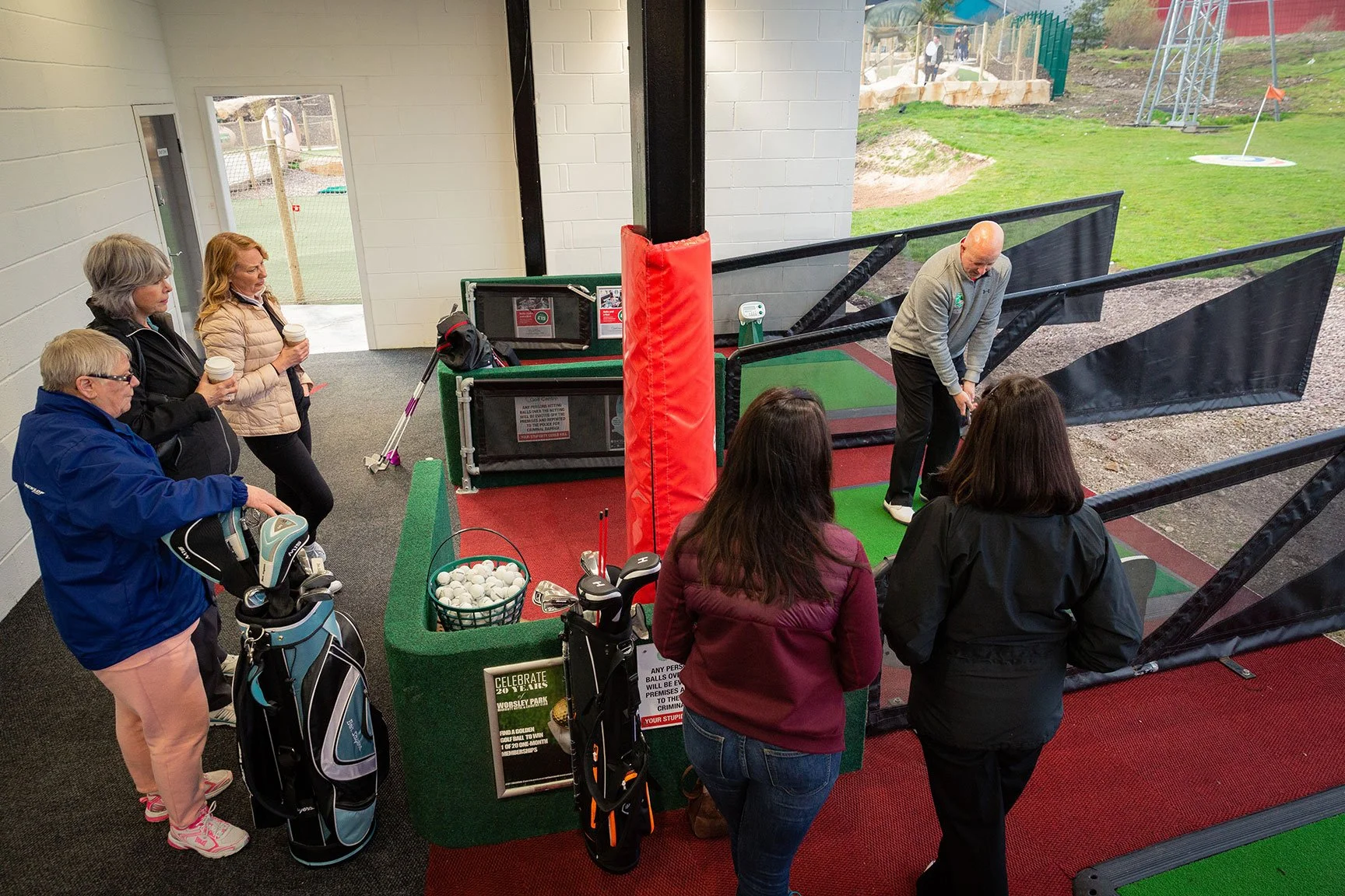 Group of people stood round a golf bay having a lesson
