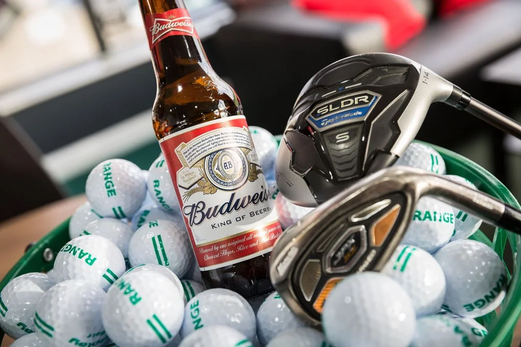 Basket of balls with golf clubs and a Budweiser