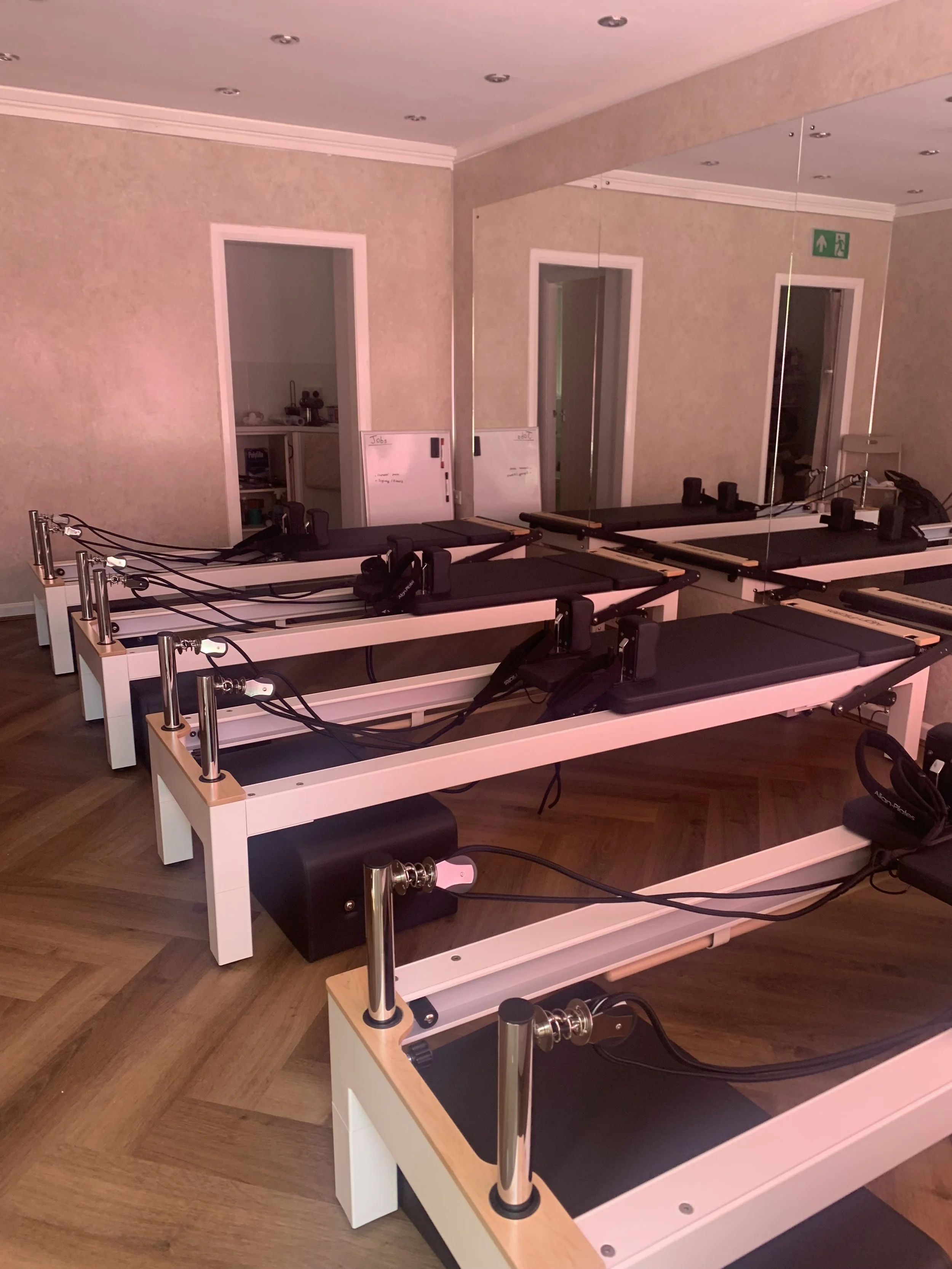 A row of reformer Pilates machines with black padded surfaces and wooden accents in a fitness room.