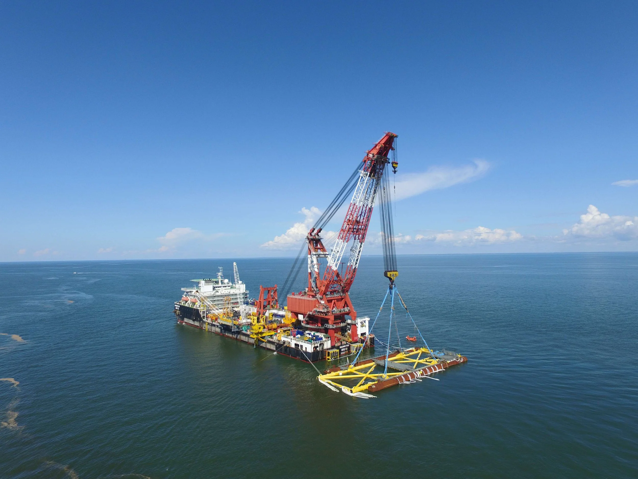 An offshore oil or gas drilling platform with a large crane is floating on the ocean under a clear blue sky.