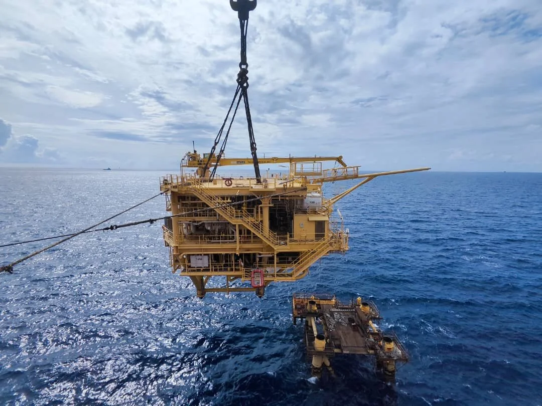 Offshore oil rig being moved into position over the ocean, with a crane lowering it into the water.