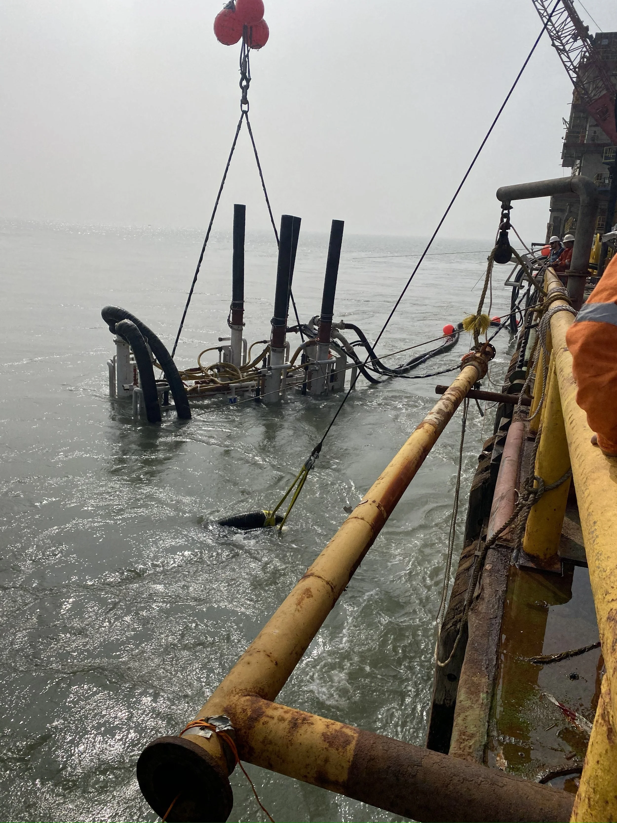 Offshore drilling rig with a submerged platform and equipment, surrounded by water, with workers in safety gear on the rig.