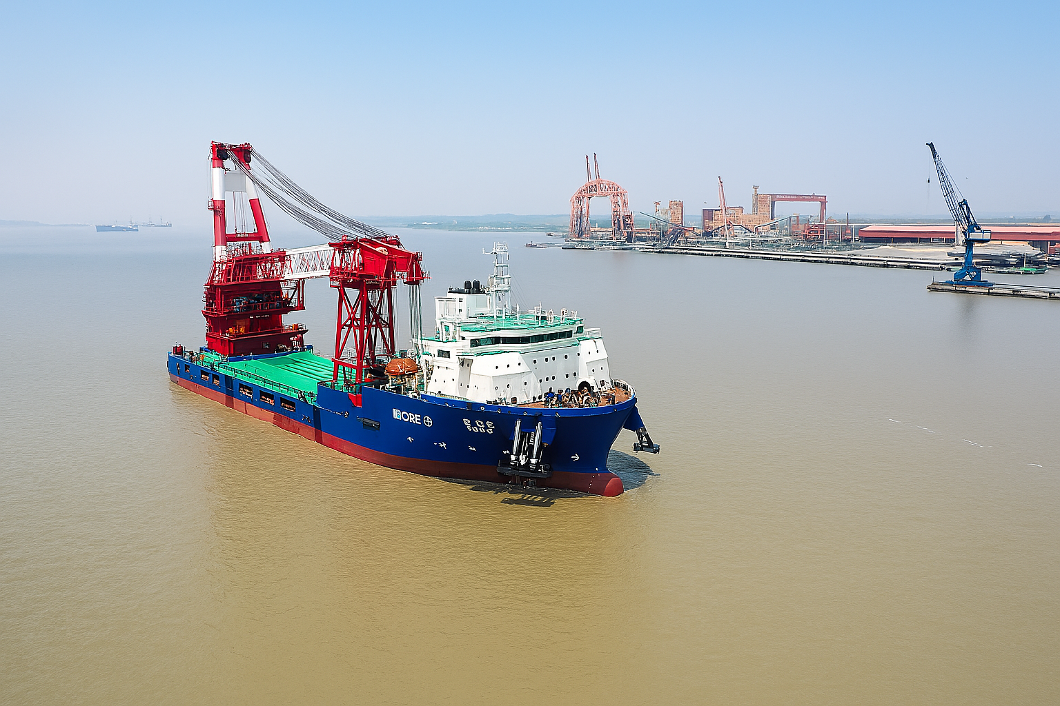 A large blue and white ship with a red crane on board navigating in a harbor near an industrial shipyard with cranes and structures in the background.