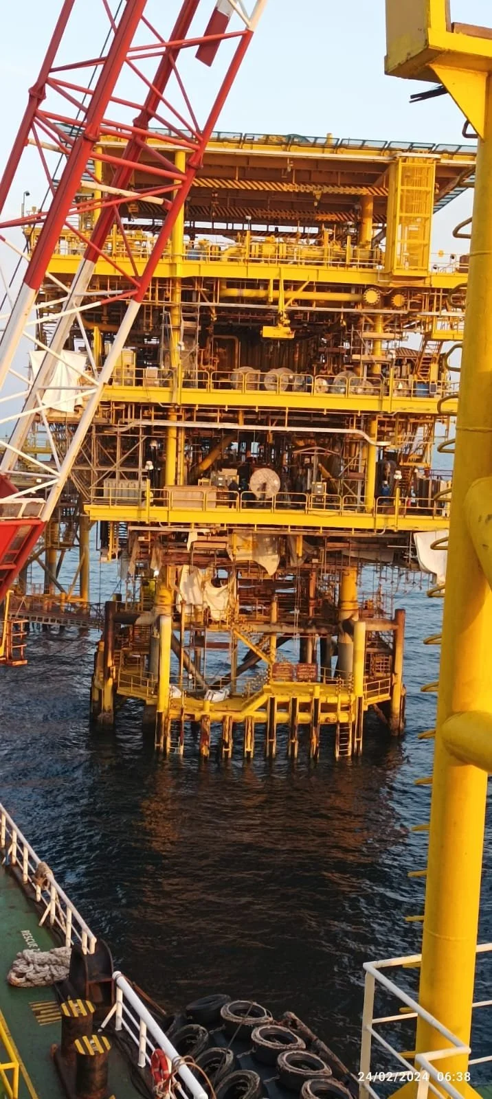 An offshore oil rig with multiple levels of yellow and brown structures on the water, surrounded by safety equipment and parts of a crane.