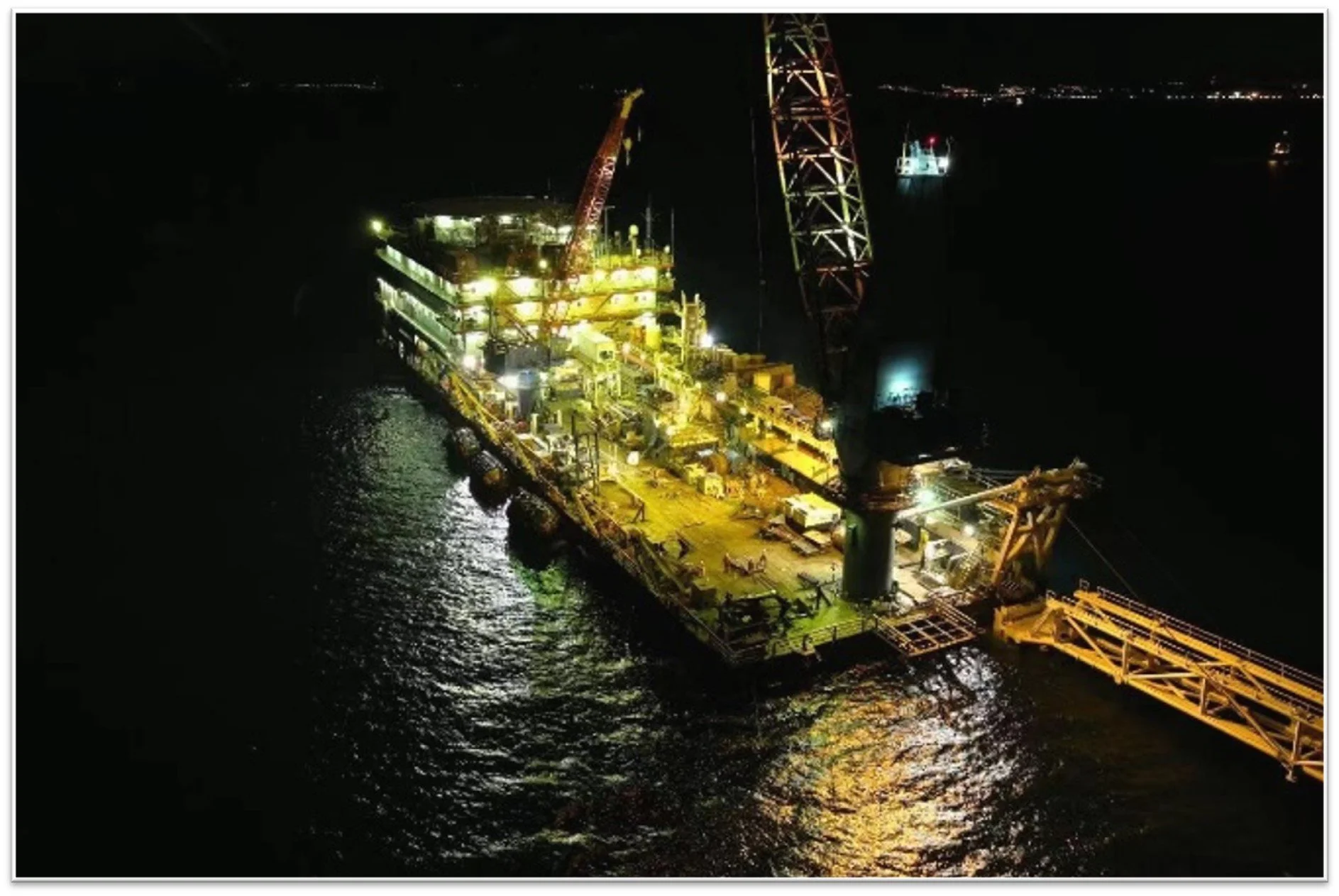 An offshore oil rig illuminated at night, with a large crane and the sea surrounding it.