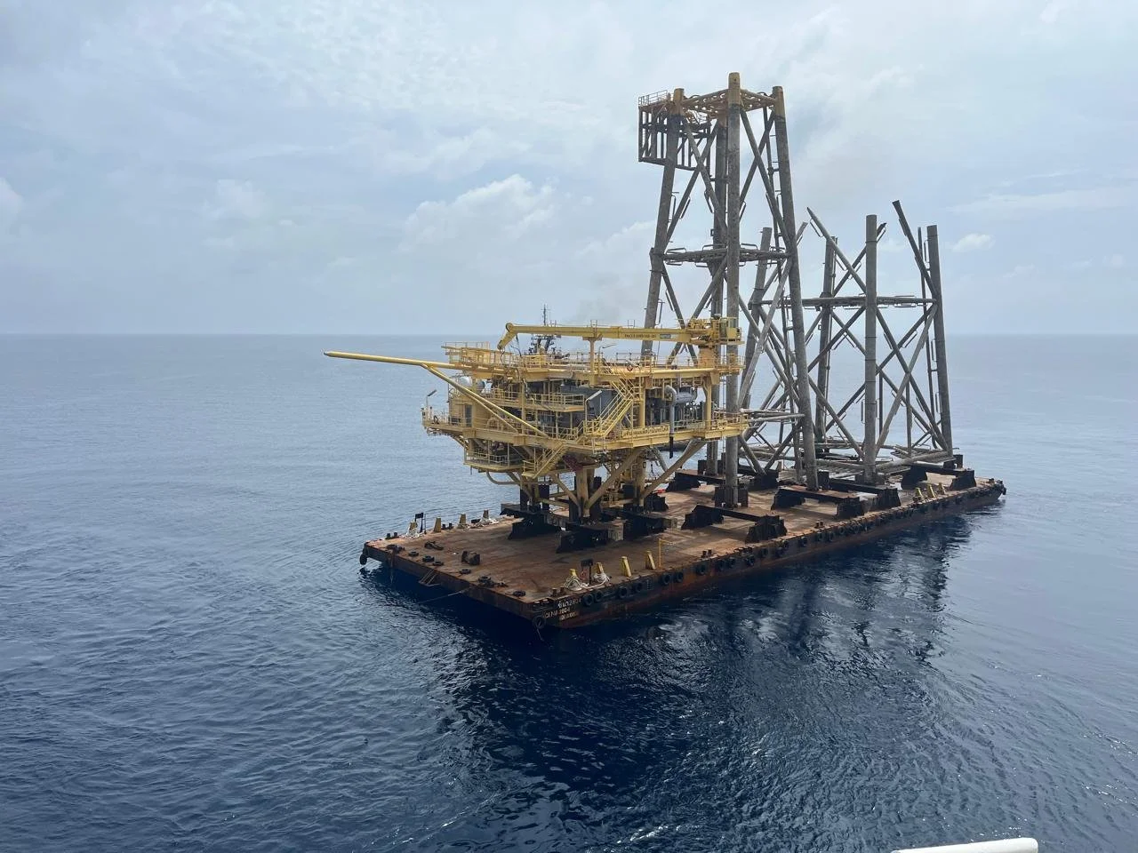An offshore oil platform floating on the ocean with a cloudy sky overhead.