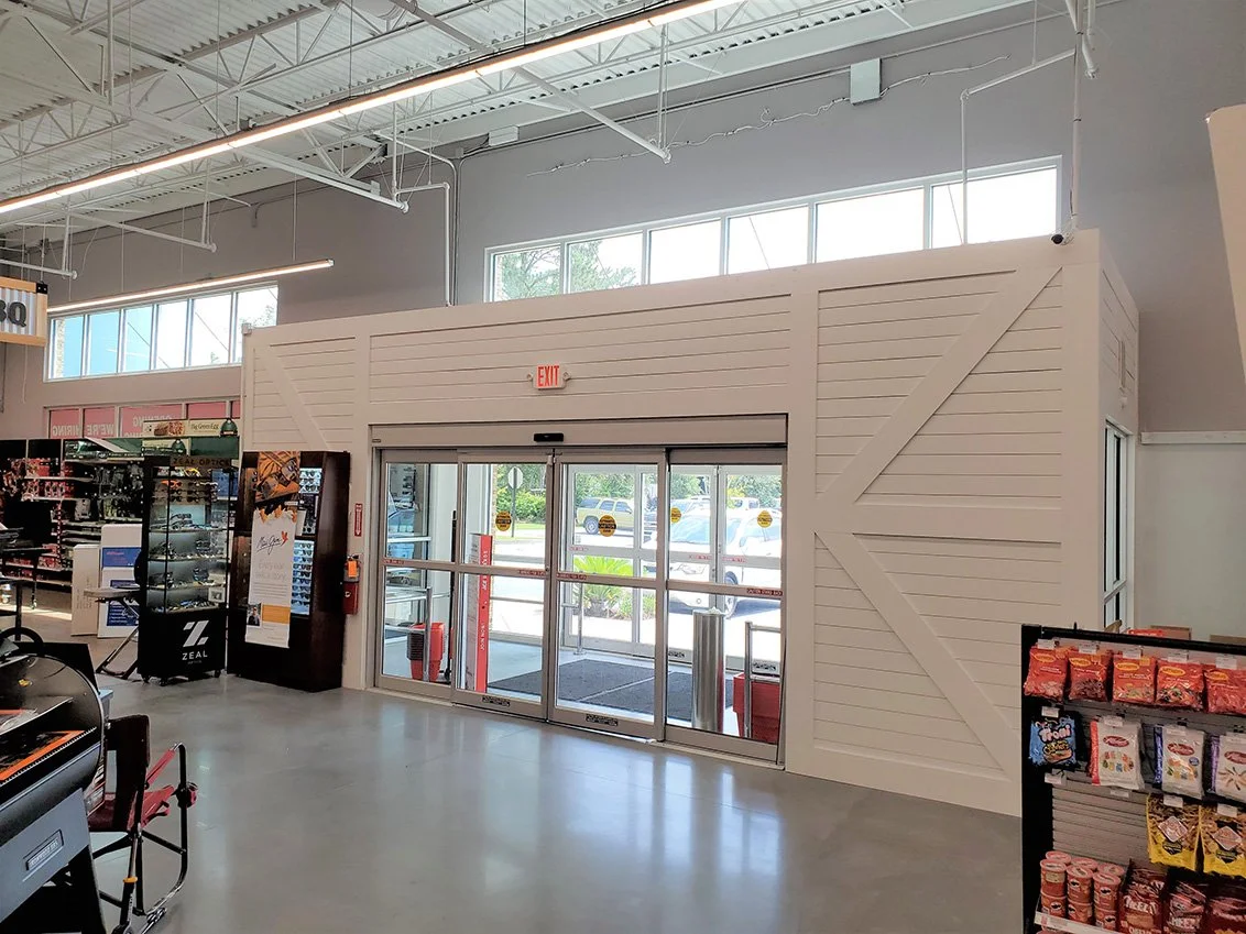 Interior of a retail store with a sliding glass door exit, shelves with snacks, and a small white building or kiosk inside the store.