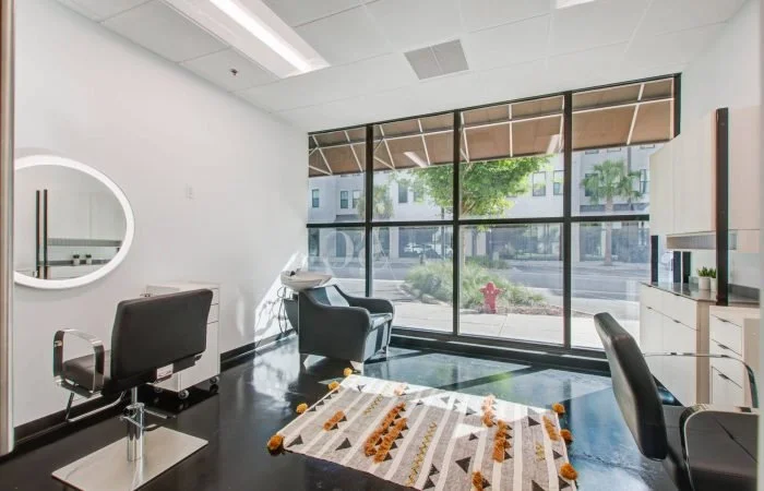 Modern hair salon with two styling chairs, a mirror, a styling station, and large windows in an urban setting.