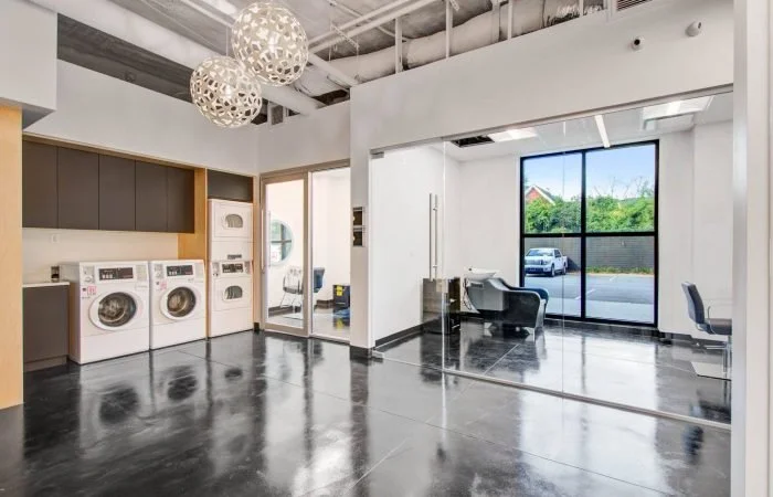 Modern laundry room with washers, dryers, and a glass wall with an office area and outside view