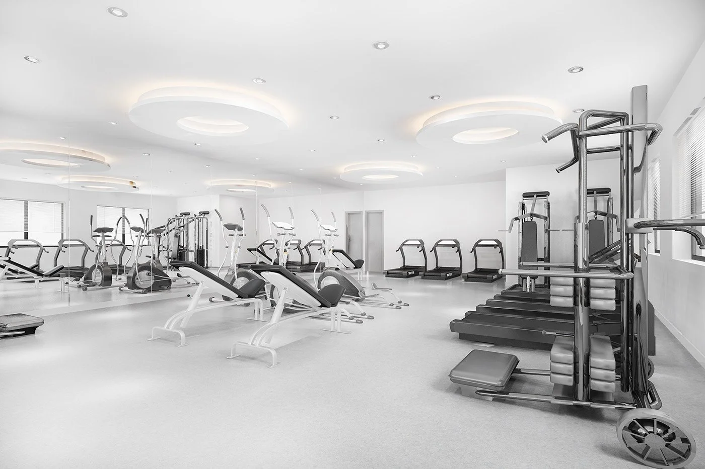 A modern, bright gym with various exercise machines including treadmills, ellipticals, and weightlifting equipment, all arranged in a spacious, well-lit room with white walls and ceiling lights.