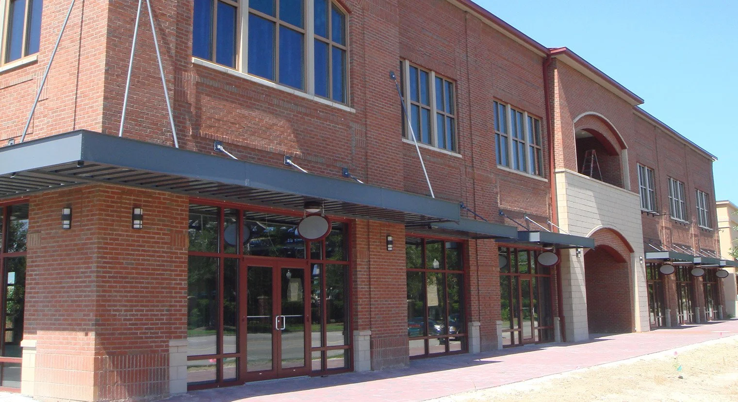 Exterior of a modern brick building with large windows, sidewalk, and some blue sky.