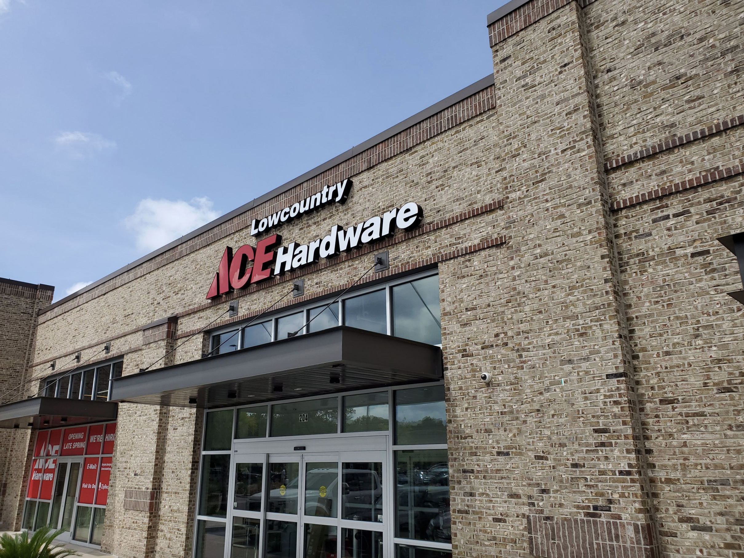 Exterior of Lowes and Ace Hardware store with brick facade, glass entrance, and signages.