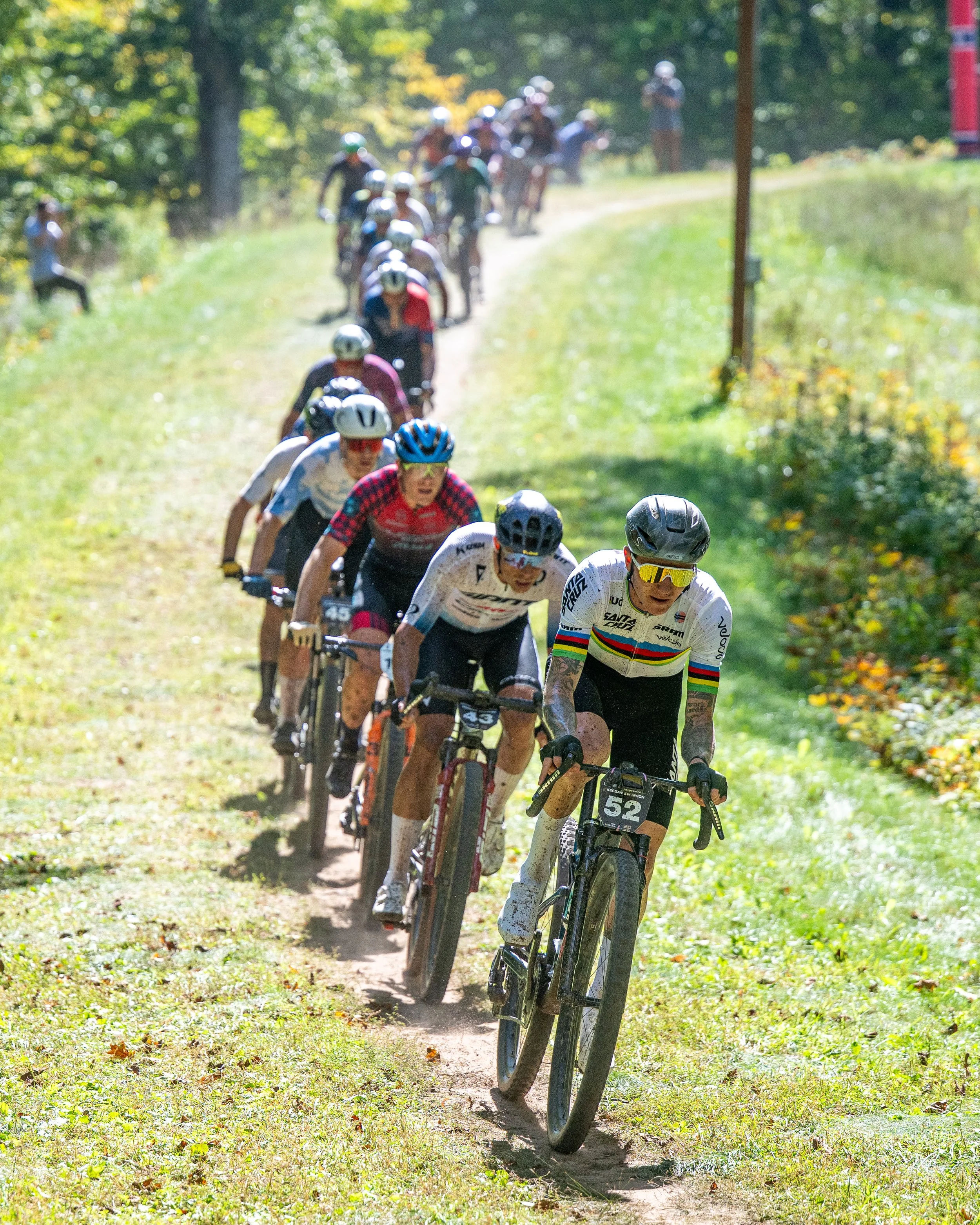 Cyclists participating in a mountain biking race along a dirt trail in a wooded area.