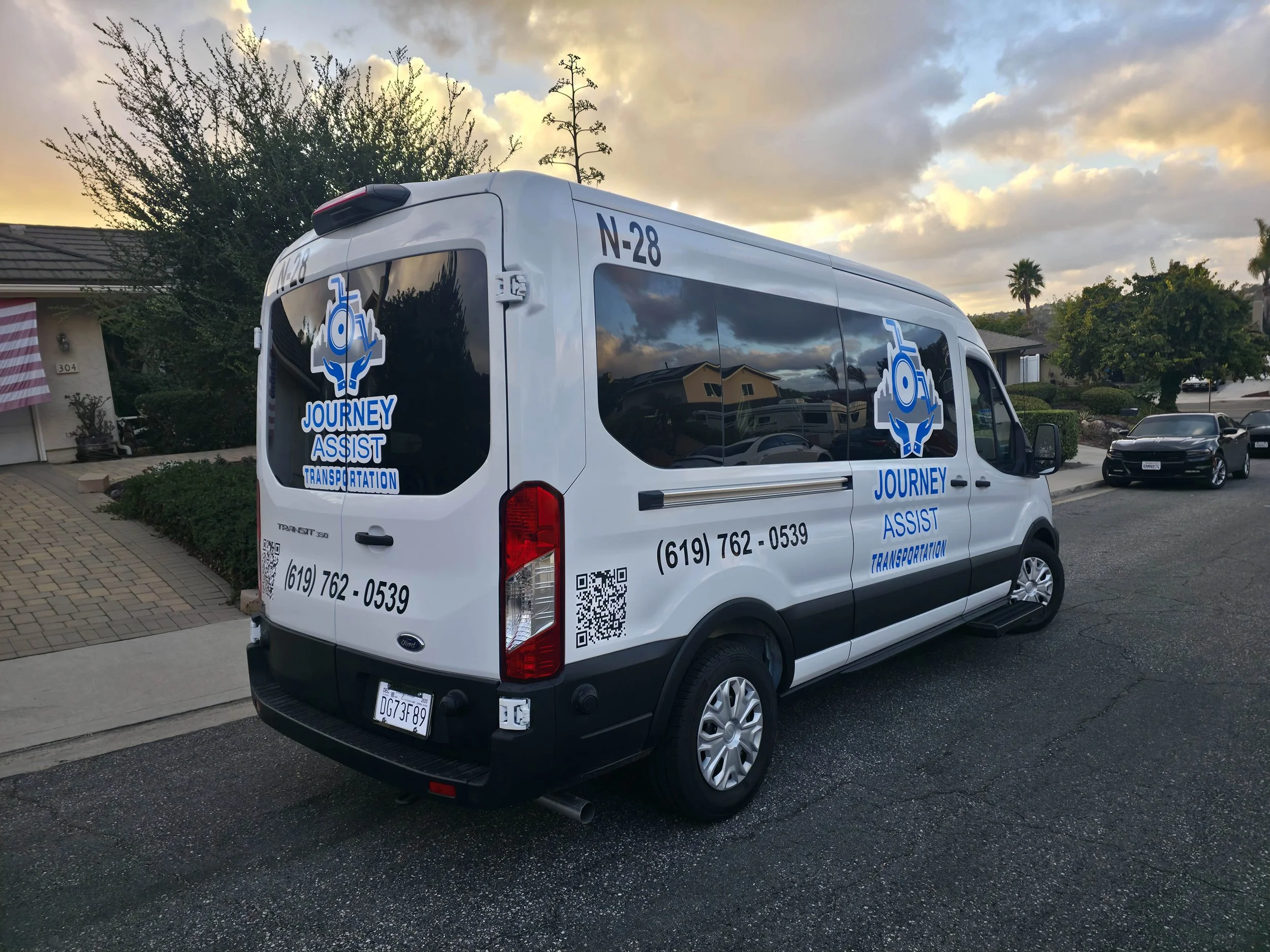 White van with logo and contact information for Journey Assist Transportation, parked on a residential street during sunset.