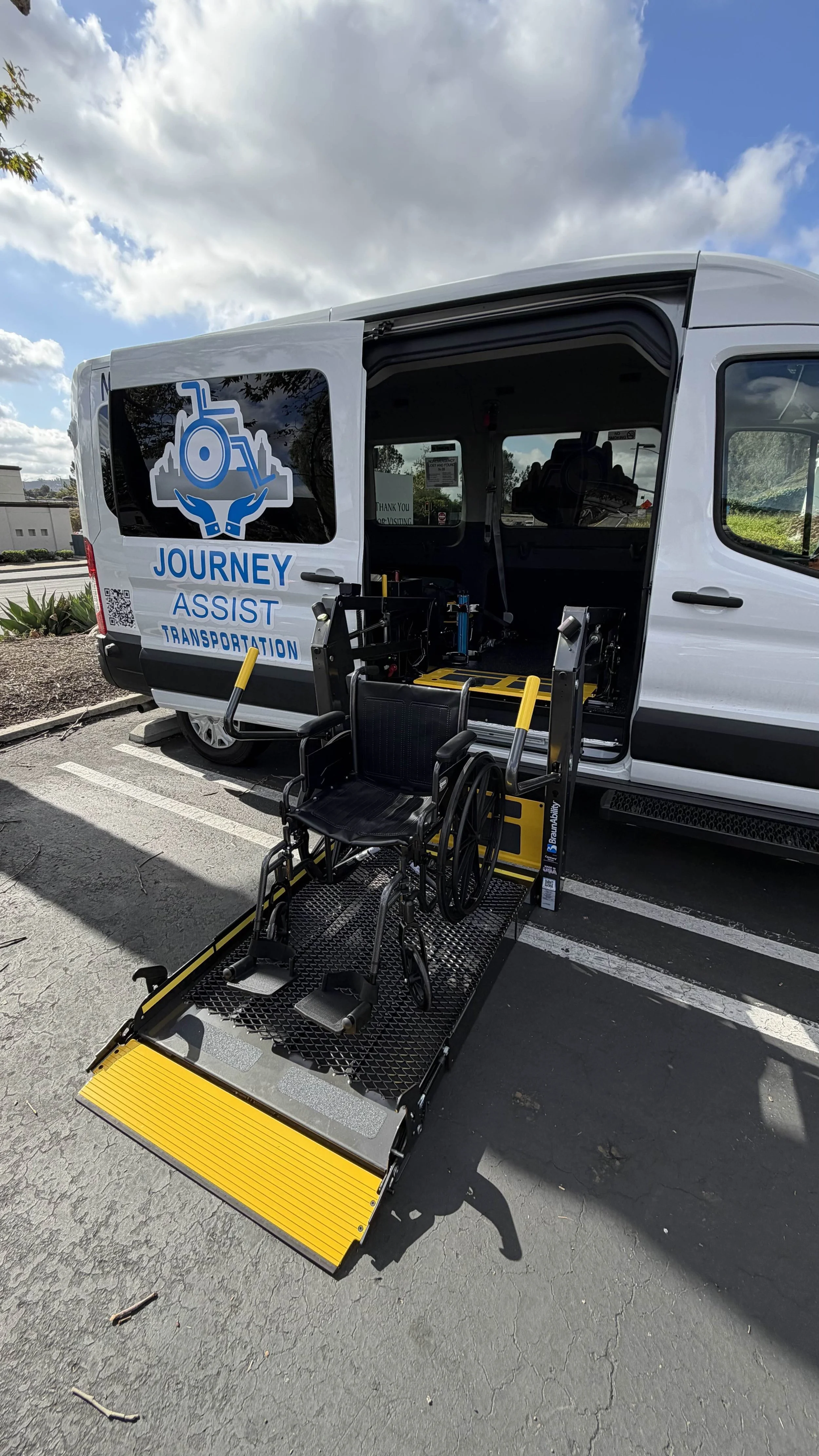 A wheelchair accessible van with a ramp extended for wheelchair entry, displaying the logo and name 'Journey Assist Transportation' on the side.