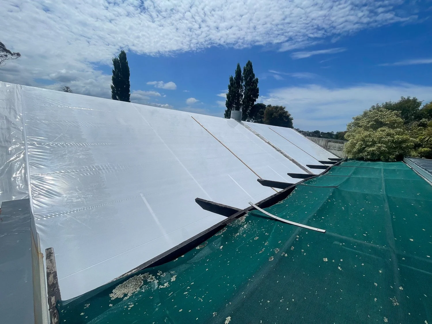 A rooftop with solar panels and a tarp covering part of it under a partly cloudy sky.