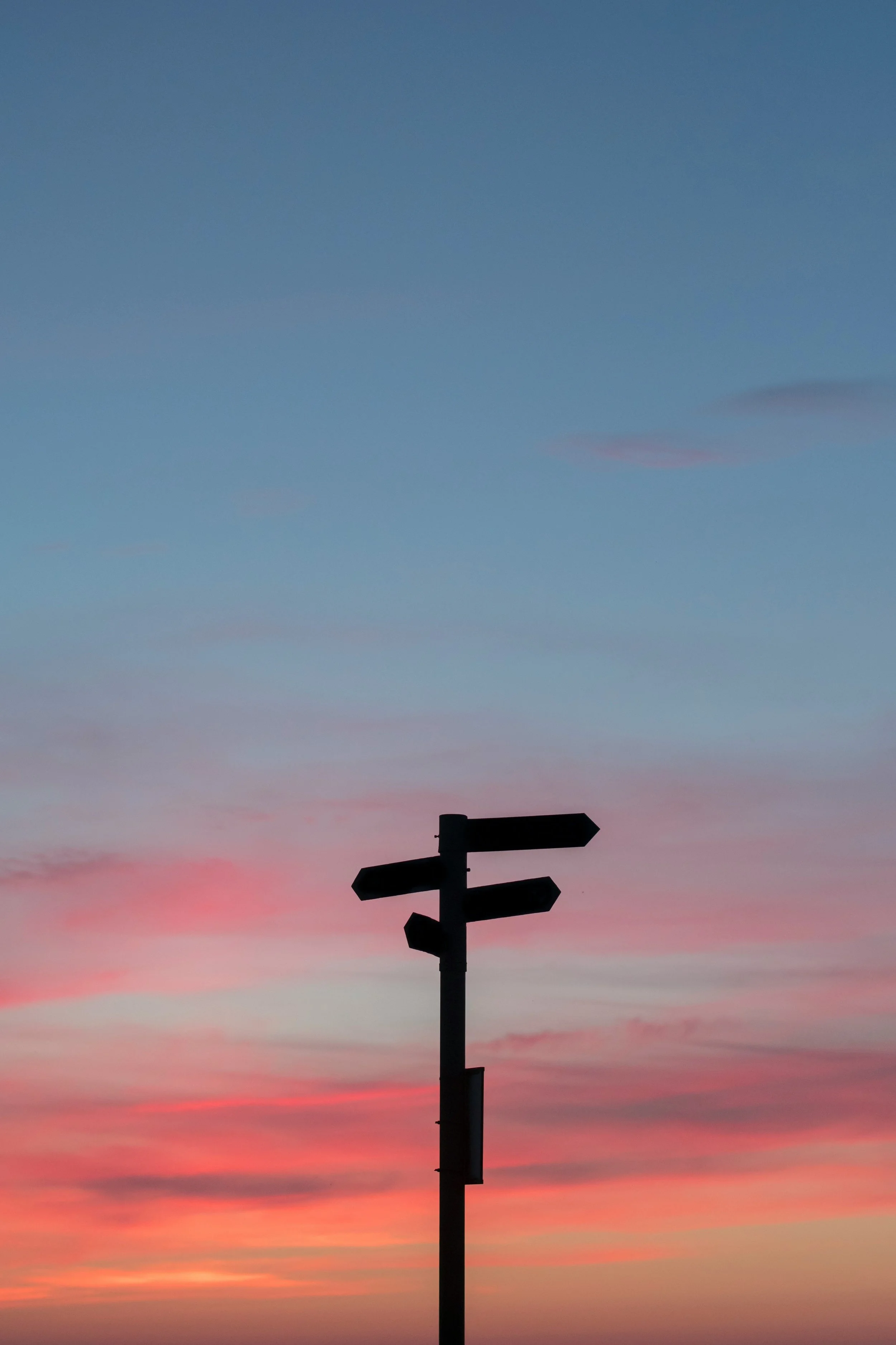 Silhouette of a signpost with multiple blank directional signs against a colorful sunset sky with pink, orange, and blue hues.