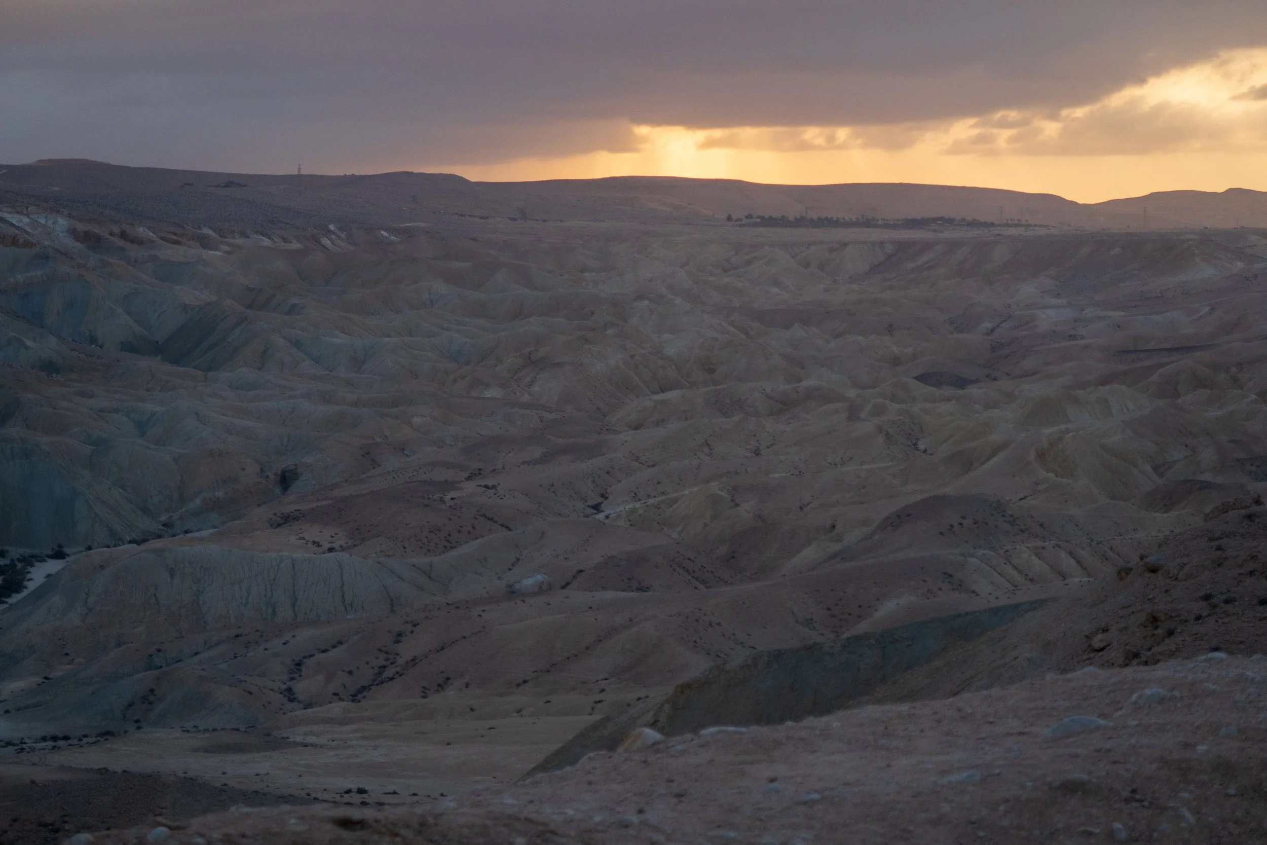 A scenic view of a desert landscape with rolling hills and a cloudy sky at sunset.