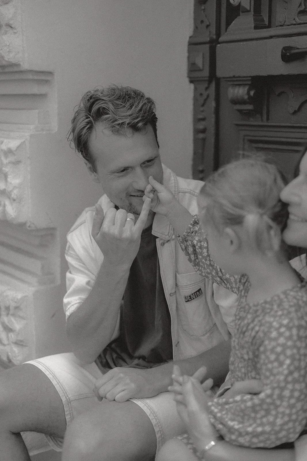 Ein Mann und ein Kind sitzen sich gegenüber. Der Mann berührt die Nase des Kindes, während das Kind seine Hand auf den Knien des Mannes legt. Sie scheinen eine intime und glückliche Verbindung zu haben.